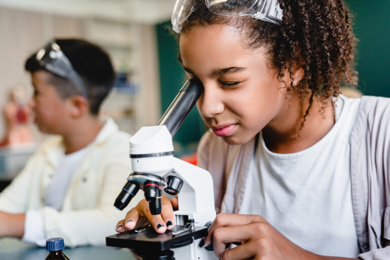 A closeup of a schoolgirl looking through a telescope in a classroom