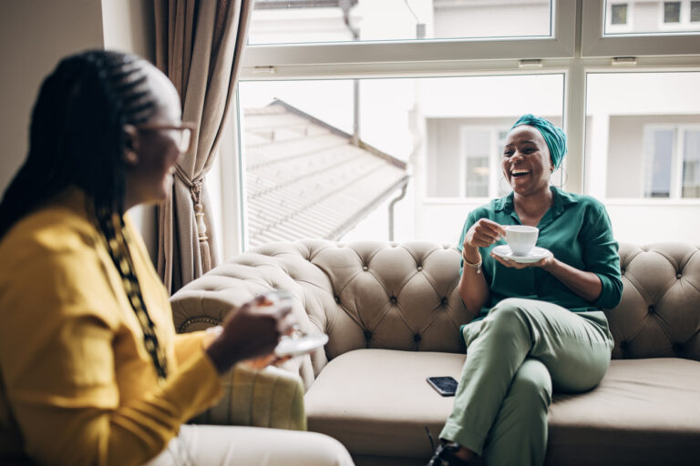 Two women talking and enjoying coffee on a couch.