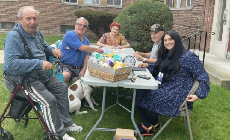 a group of smiling people sitting at a picnic table outside