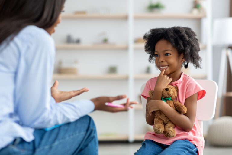 A smiling child sitting in a chair and speaking with a therapists