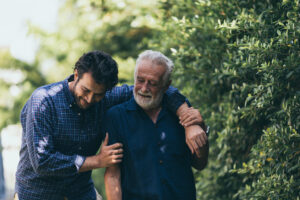 An elderly man and his son are smiling and walking in the park.